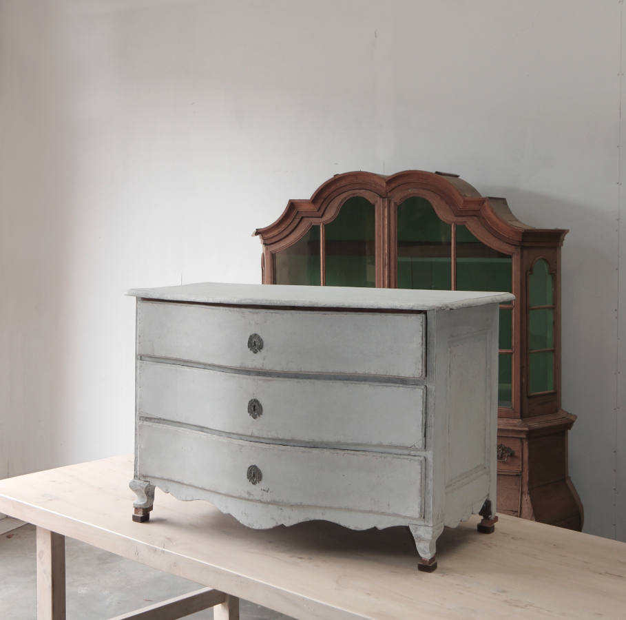 An early 18th century serpentine commode with three drawers and chalky paint finish
