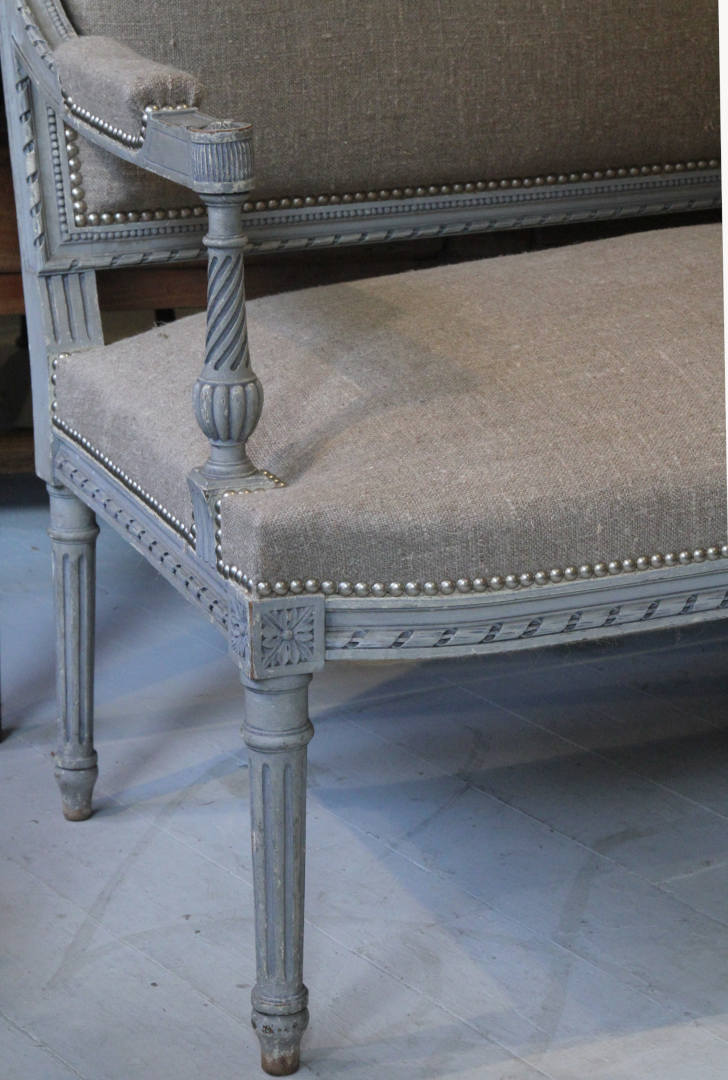 A close up view showing the left hand side of a French sofa with Louis XVI carving
